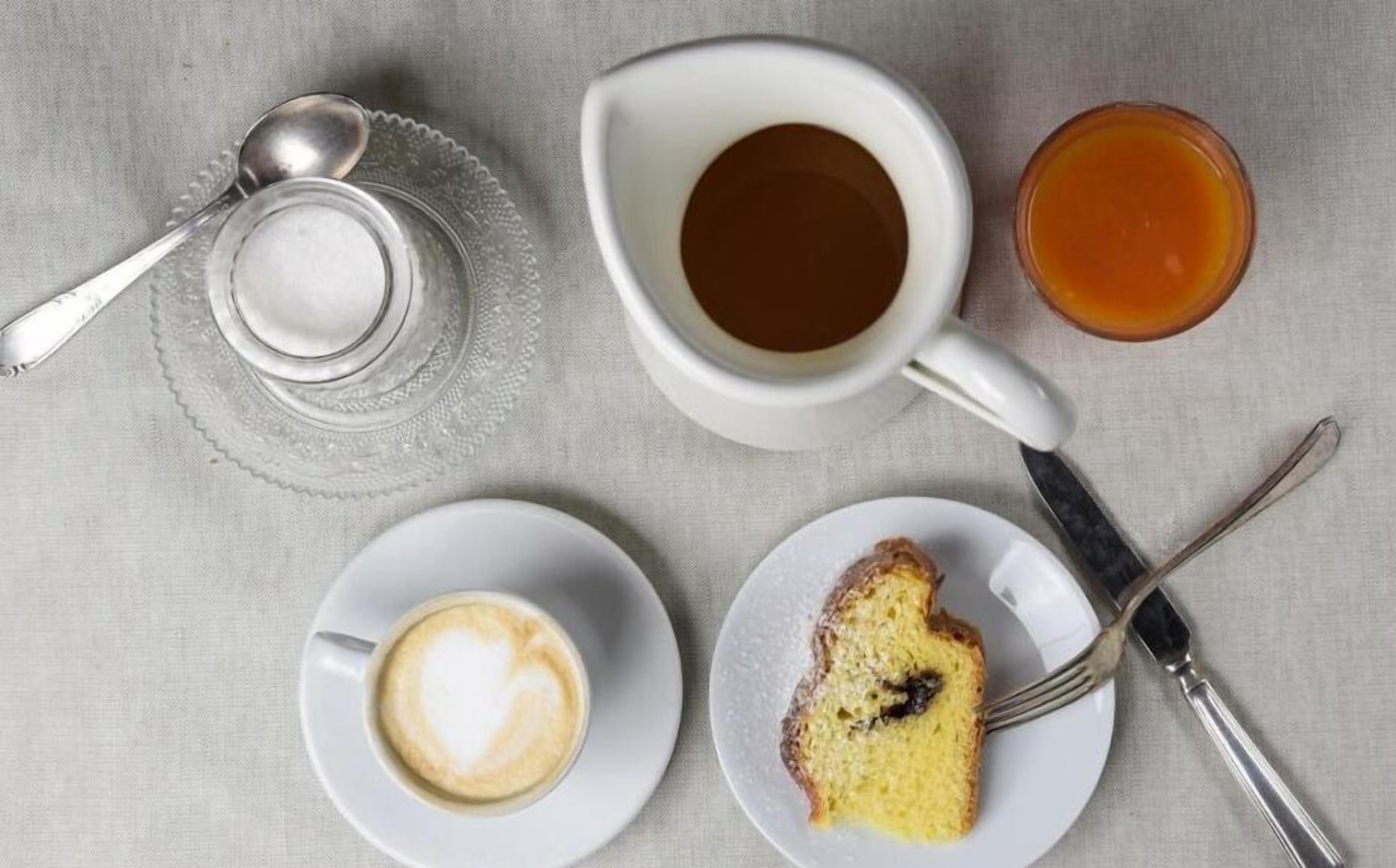 Una mesa dispuesta con una taza de café, un vaso de agua, un vaso de té y una porción de pastel.