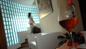A glass of red wine with a strawberry on the rim, a white tablecloth, and a window with a grid pattern. - Albergo Scaldaferro (Sandrigo)
