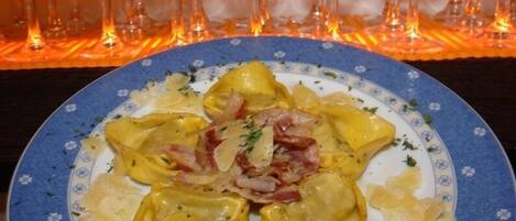 Un plato de ravioles, adornado con cebollas y hierbas, servido en un plato azul y blanco con motivos florales.