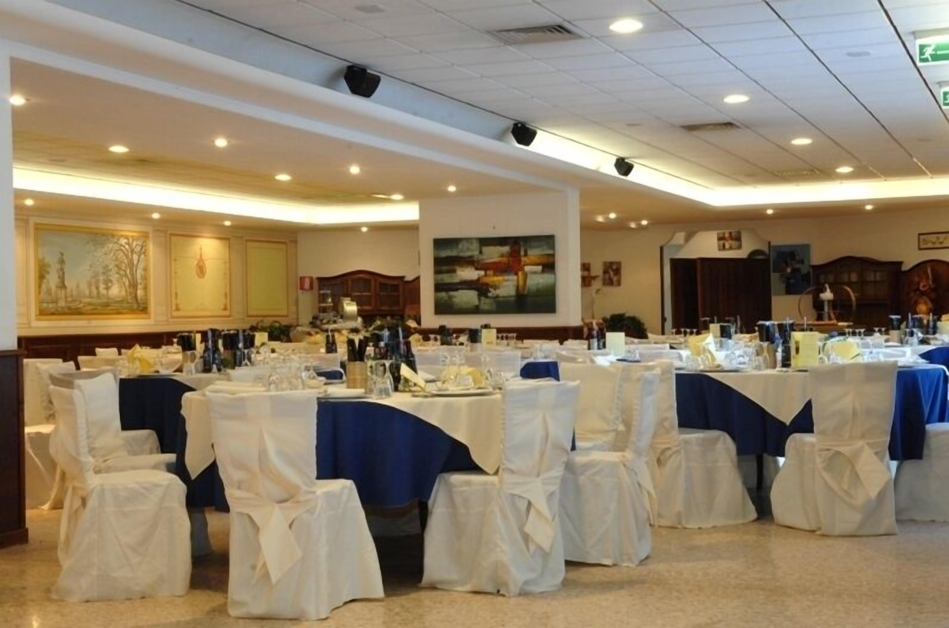 Una sala da banchetti con tavoli rotondi ricoperti da tovaglie bianche e centrotavola blu, disposti in file.