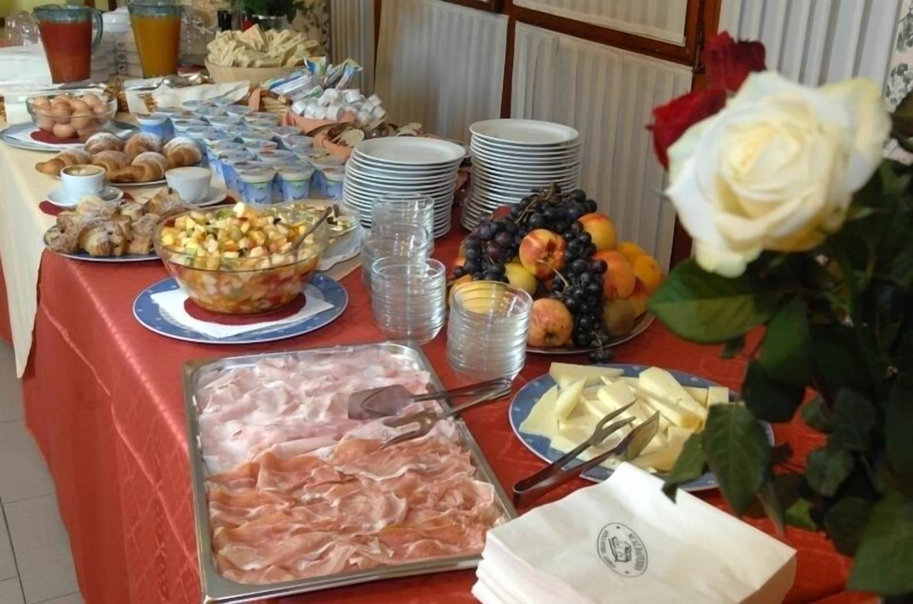 Una mesa de buffet con diversos alimentos, como frutas, pastelería y carnes, junto con platos apilados y vasos transparentes.