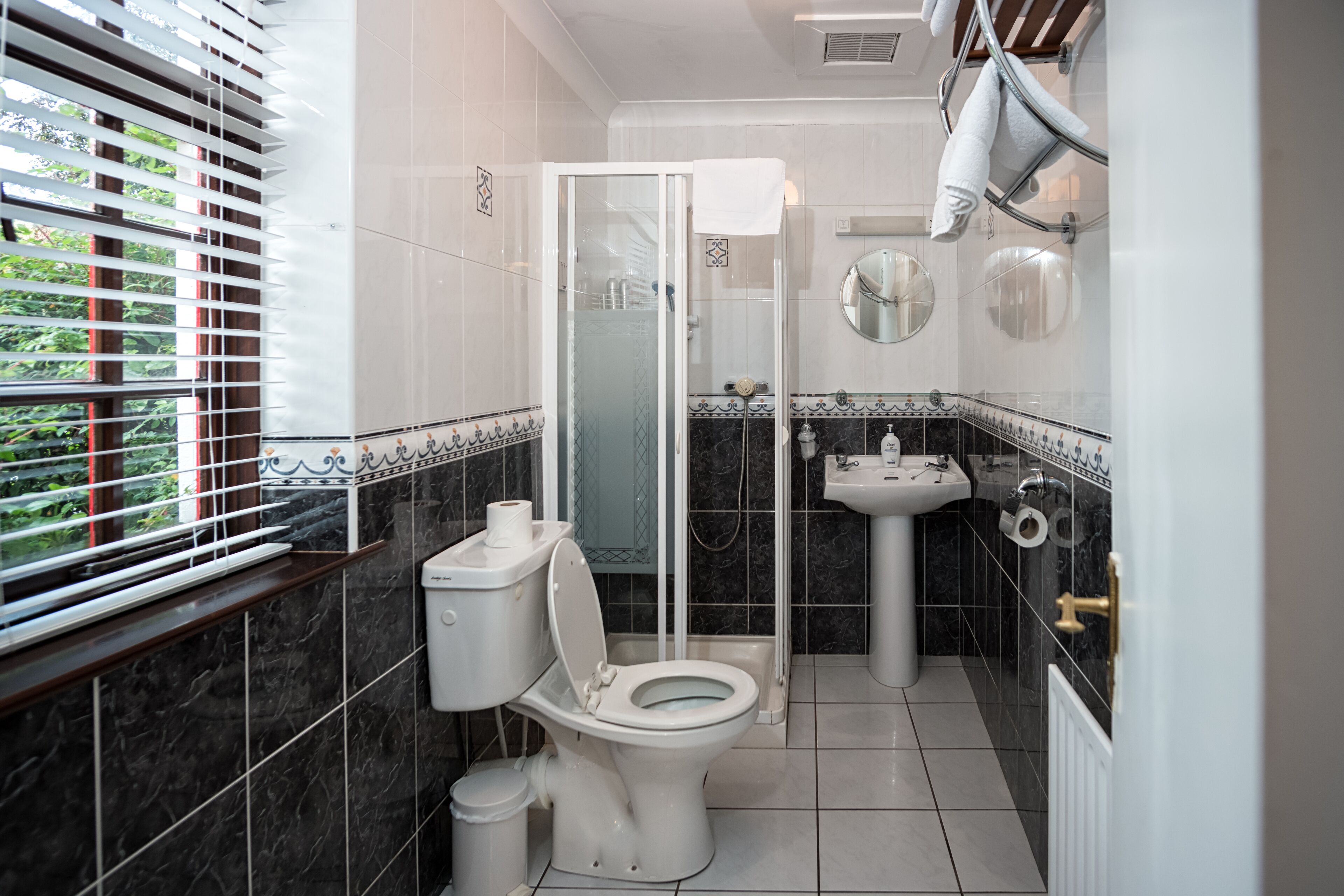 Un baño con inodoro, ducha, lavamanos y ventana con persianas.