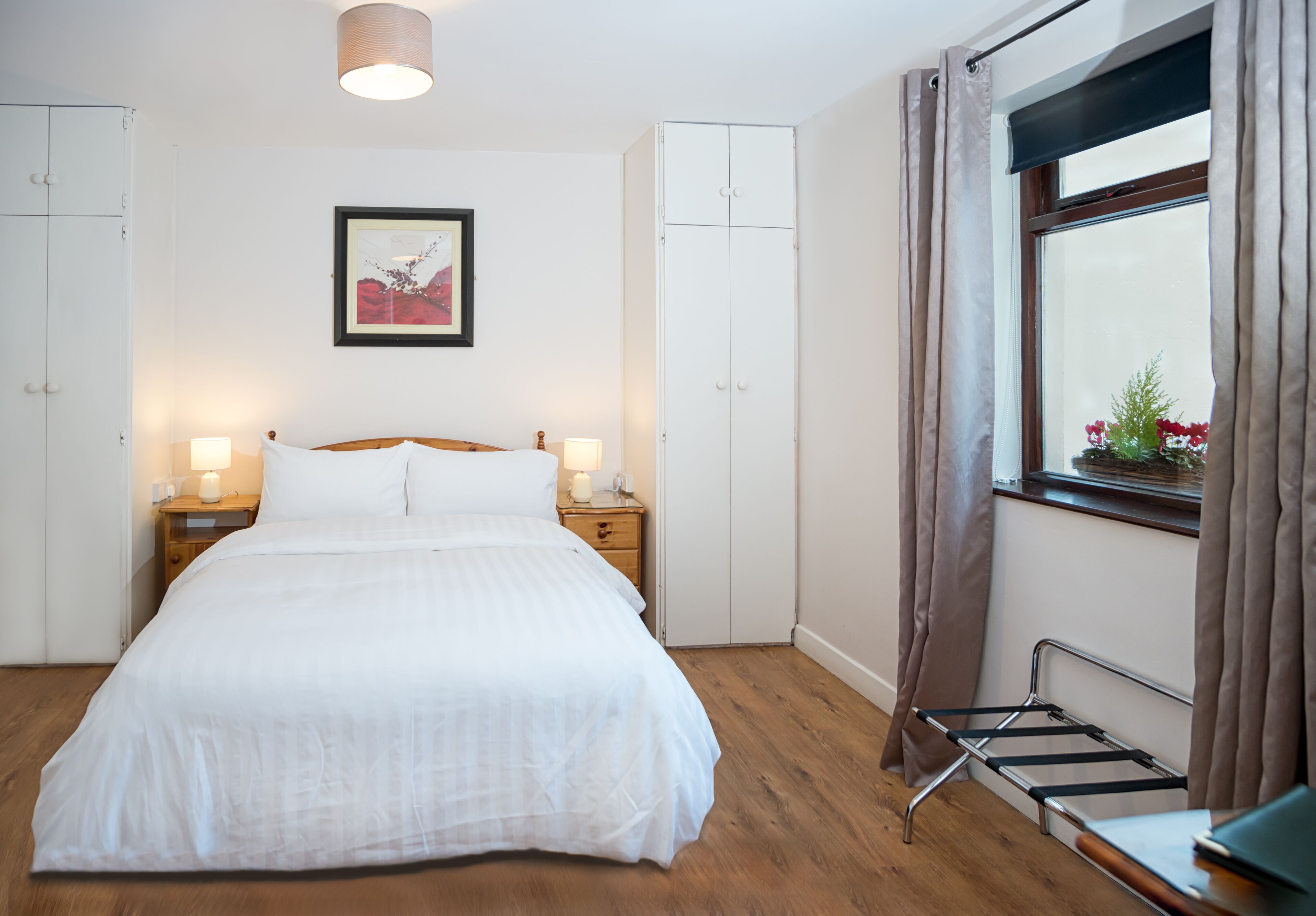 A neatly arranged bedroom with a bed, bedside tables, a hanging laundry rack, and a window with curtains.