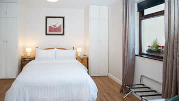 A neatly arranged bedroom with a bed, bedside tables, a hanging laundry rack, and a window with curtains.
