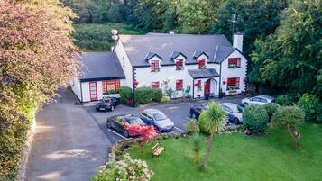 A white building with red accents, multiple cars parked in front, and lush greenery surrounding the property.