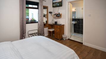 Een slaapkamer met een bed, een houten dressoir, een bureau, een spiegel, een televisie en een badkamer die door een geopende deur zichtbaar is.