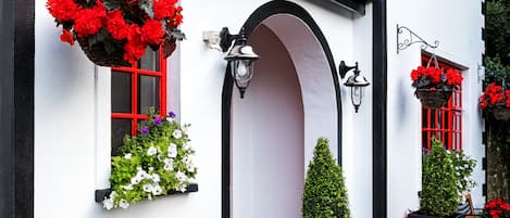 Un edificio blanco con detalles negros, ventanas de marco rojo y macetas colgantes de flores.