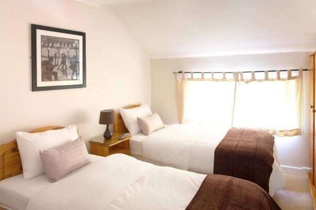 A hotel room with two beds, a nightstand with a lamp, a framed picture on the wall, and a window with curtains.