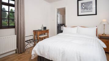 A bedroom with a bed, a wooden nightstand, a lamp, a radiator, a window with curtains, and a framed picture on the wall.
