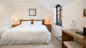 A bedroom with a large bed, bedside lamps, a wooden desk, and a window with a view. - Woodside Lodge (Westport)