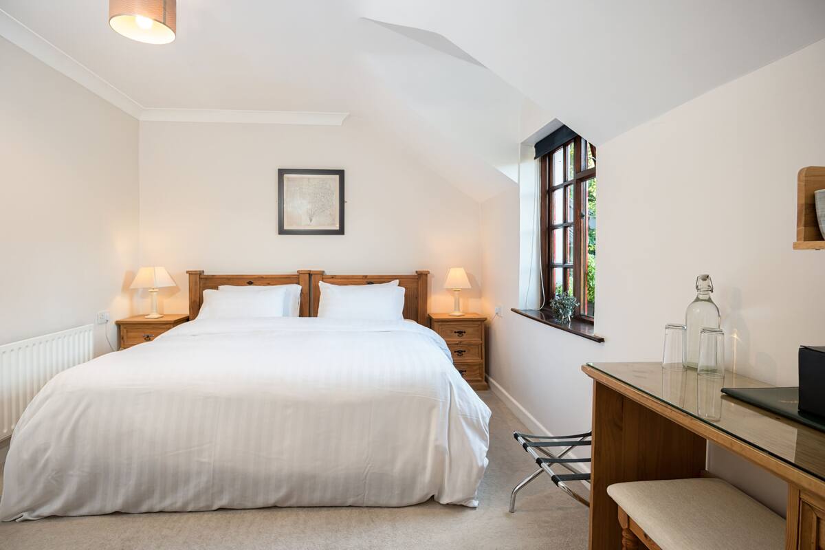 A bedroom with a large bed, bedside lamps, a wooden desk, and a window with a view.