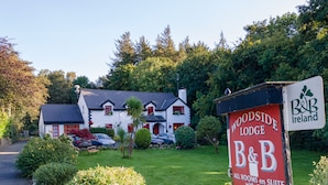 A B&B sign for Woodside Lodge with a white building and red accents, surrounded by greenery. - Woodside Lodge (Westport)