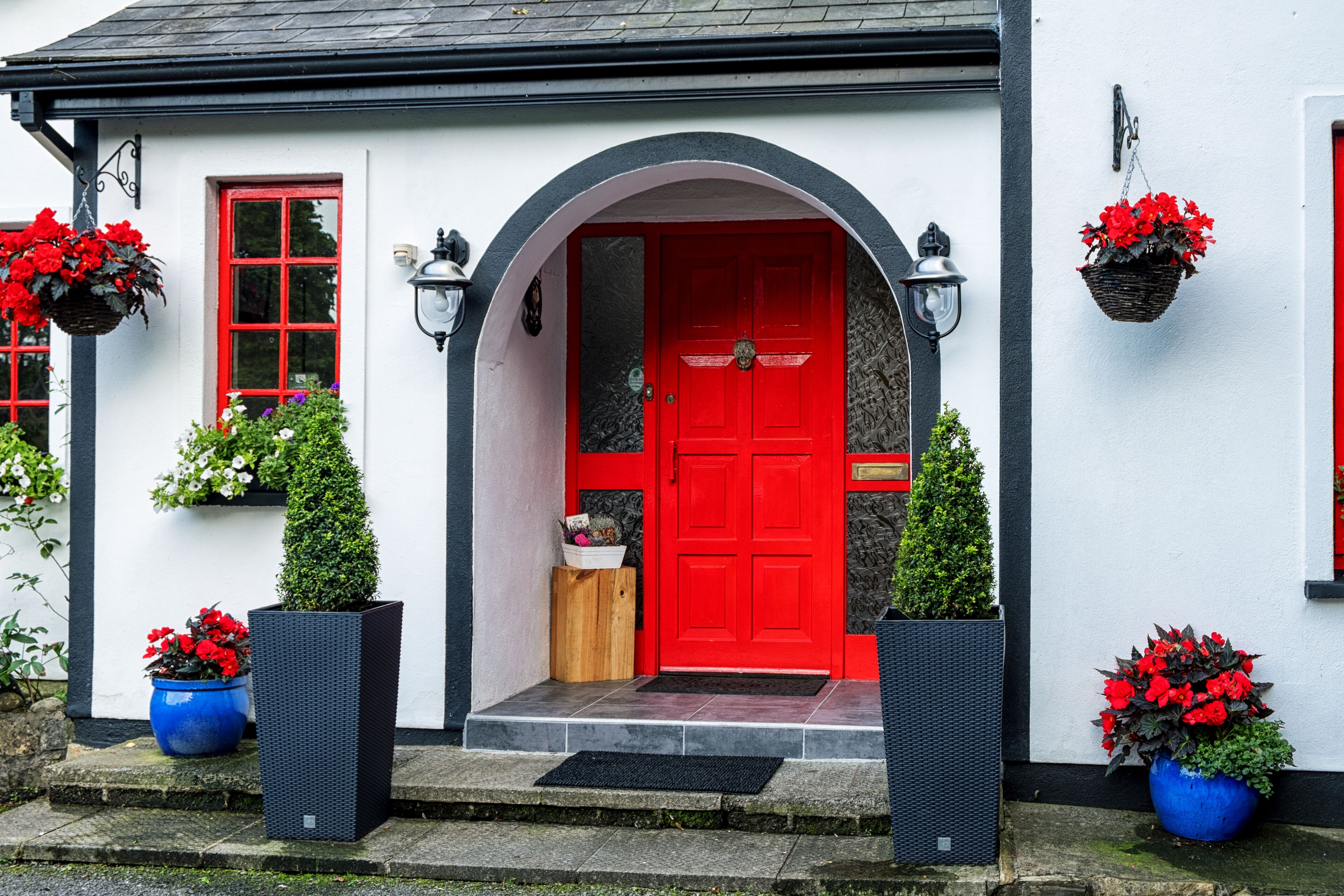 A white building with a red door, black-framed windows, and a black awning over the entrance.