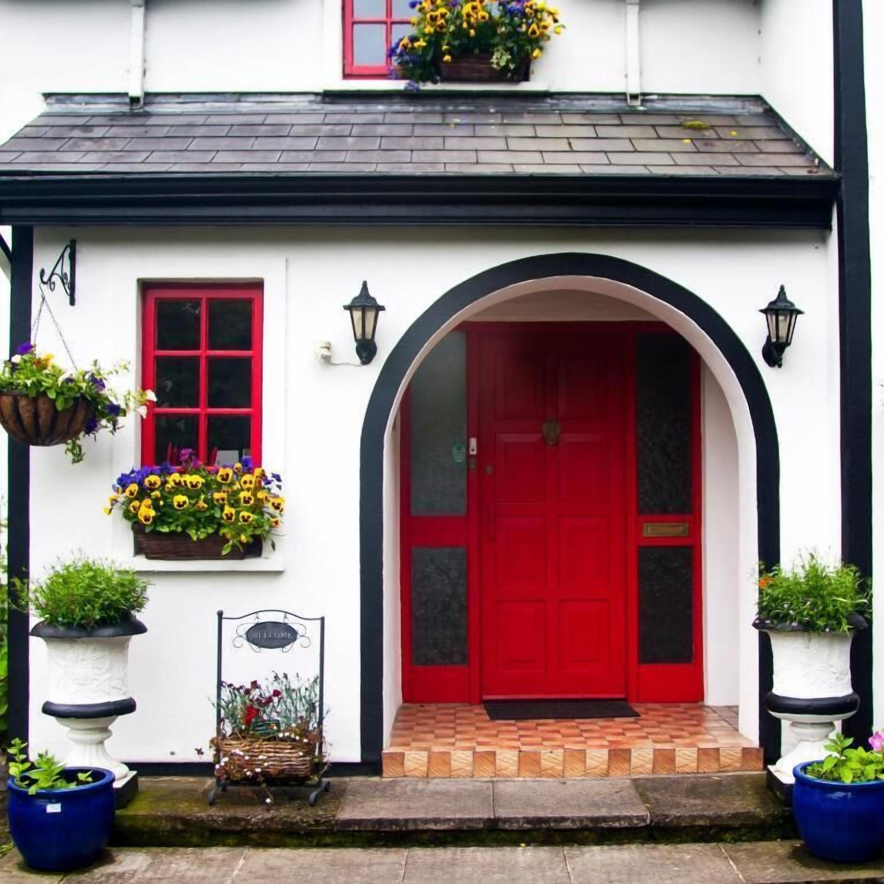 Un edificio blanco con puerta roja, ventana de marco negro y acceso con azulejos.