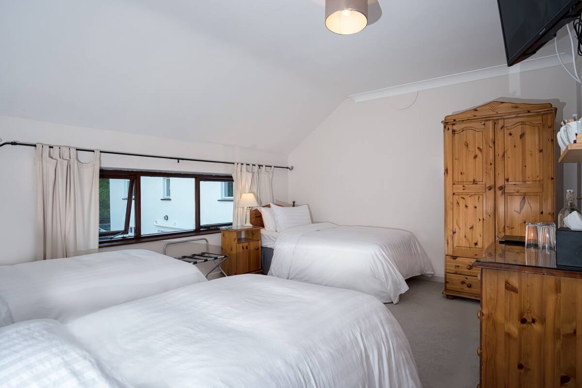 A bedroom with two beds, a wooden wardrobe, a window with curtains, and a bedside lamp.