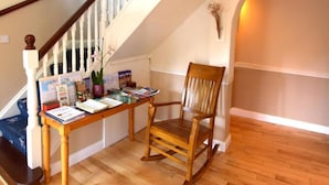 A wooden rocking chair in a room with a wooden floor, a staircase with white railings, and a wall-mounted light fixture. - Woodside Lodge (Westport)
