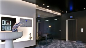 A modern hotel lobby with a reception desk, a digital display, a chair, and an elevator. - B-aparthotel Regent (Brussels)
