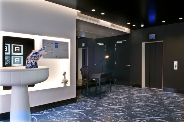 A modern hotel lobby with a reception desk, a digital display, a chair, and an elevator. - B-aparthotel Regent (Brussels)
