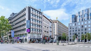 A modern hotel with a geometric facade, multiple floors, and a prominent entrance with a blue sign. - B-aparthotel Regent (Brussels)
