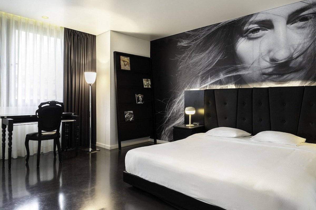 A modern hotel room with a large bed, a desk, and a chair.