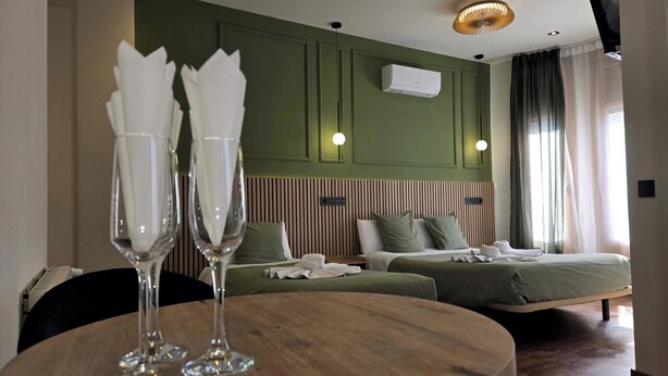 A hotel room with a bed, bedside tables, a round wooden table with two glasses, a wall-mounted air conditioner, and a ceiling light fixture. - Main Street Madrid (Madrid)