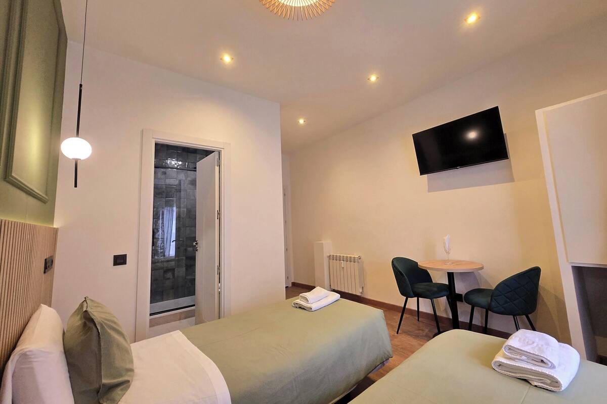 A hotel room with two beds, a television, a dining table with chairs, and a ceiling light fixture.