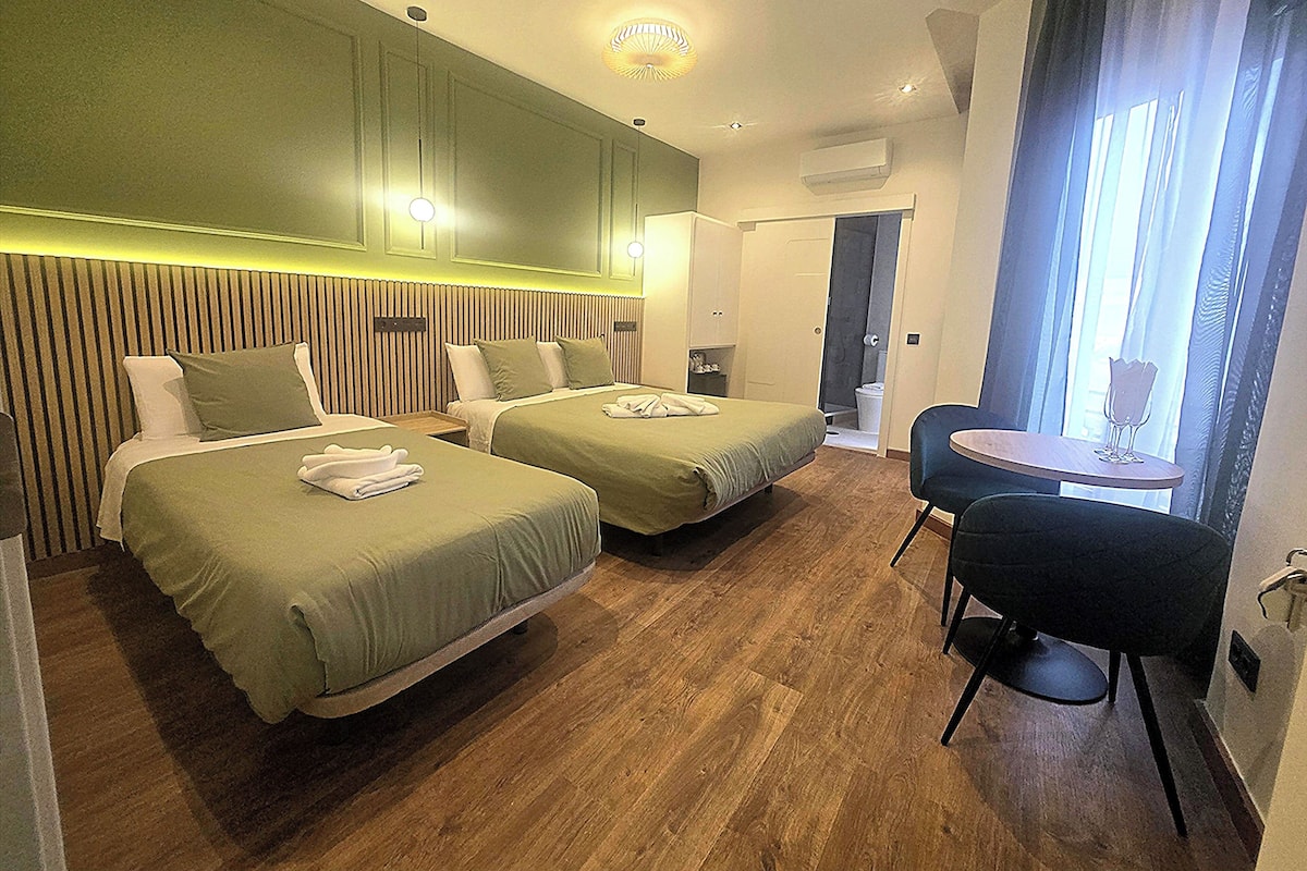 A hotel room with two beds, a small table, and a shower area.