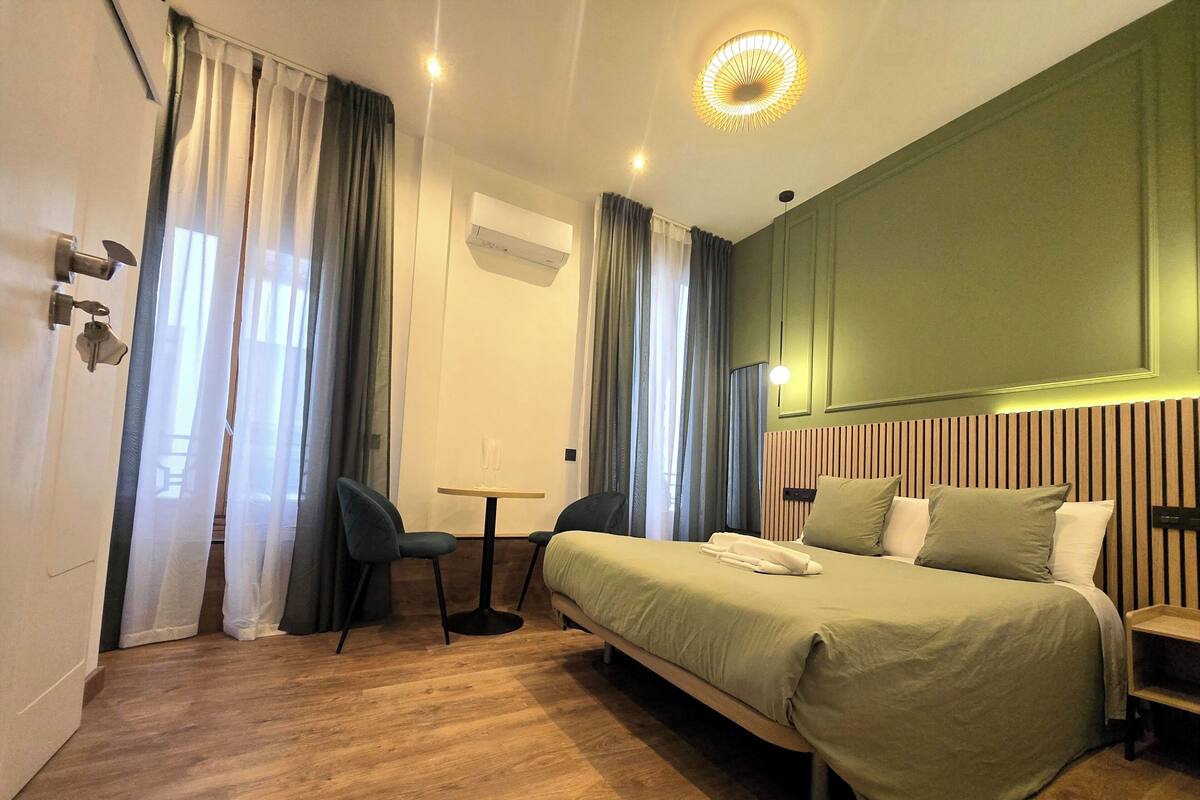 A hotel room with a bed, a desk, a chair, and a small table.