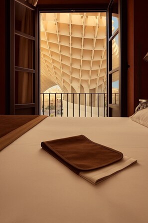 Habitación de hotel con una cama grande, vistas de un edificio a través de un muro de cristal y un balcón con un diseño de techo singular.