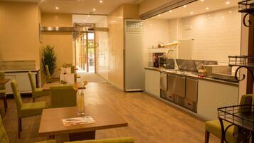 Um restaurante com piso de madeira, cadeiras estofadas em verde, uma mesa de jantar central e uma área de cozinha com eletrodomésticos de aço inoxidável.