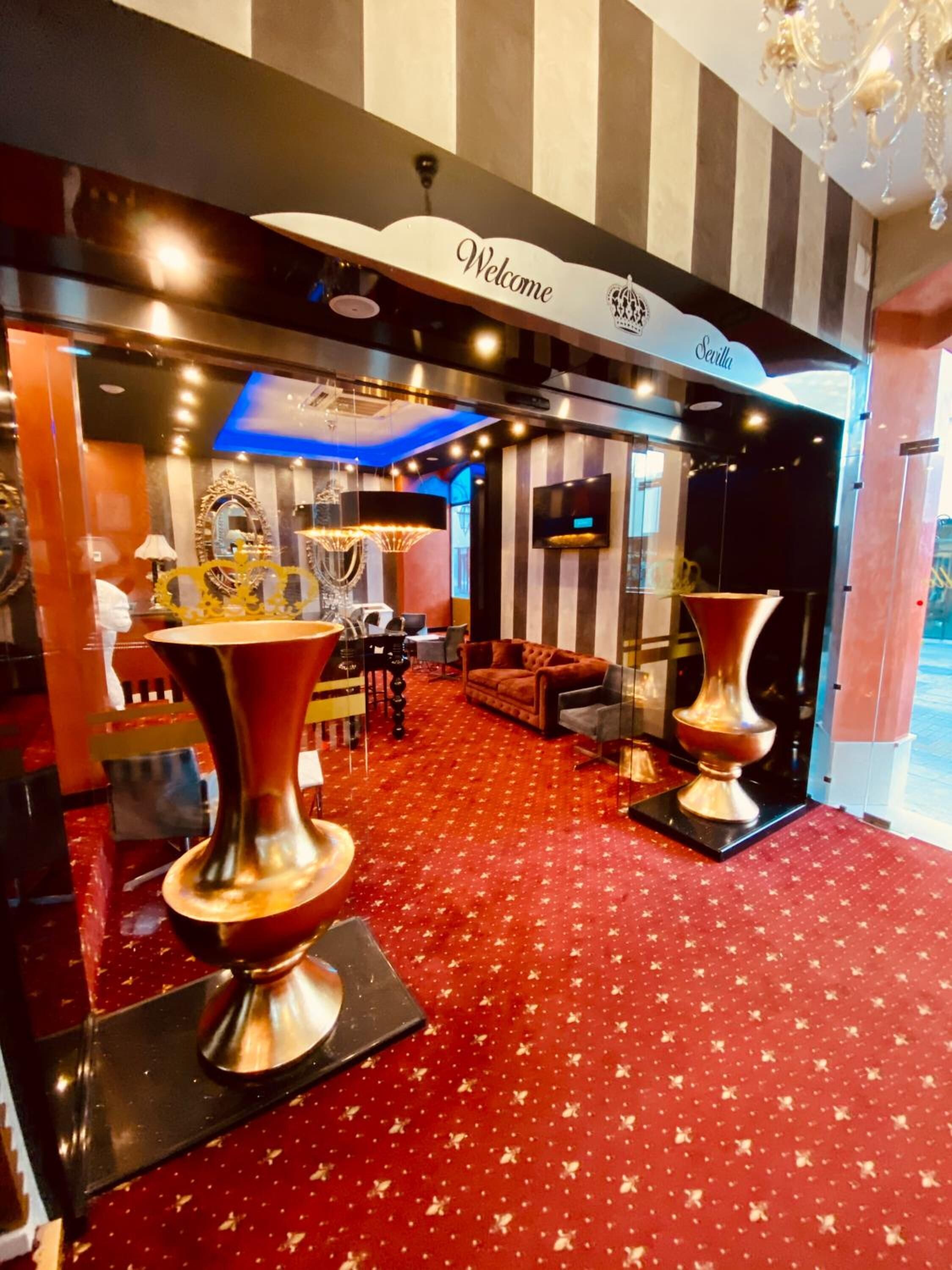 A hotel lobby with a red carpet, a 'Welcome' sign, and a 'Sevilla' sign above the entrance.