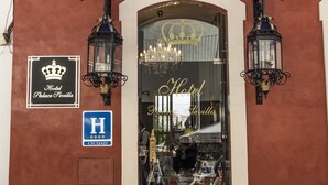 Entrada de un hotel con un letrero que indica que es un hotel, un logotipo con una corona y un símbolo de 'H' para accesibilidad para personas con discapacidad.