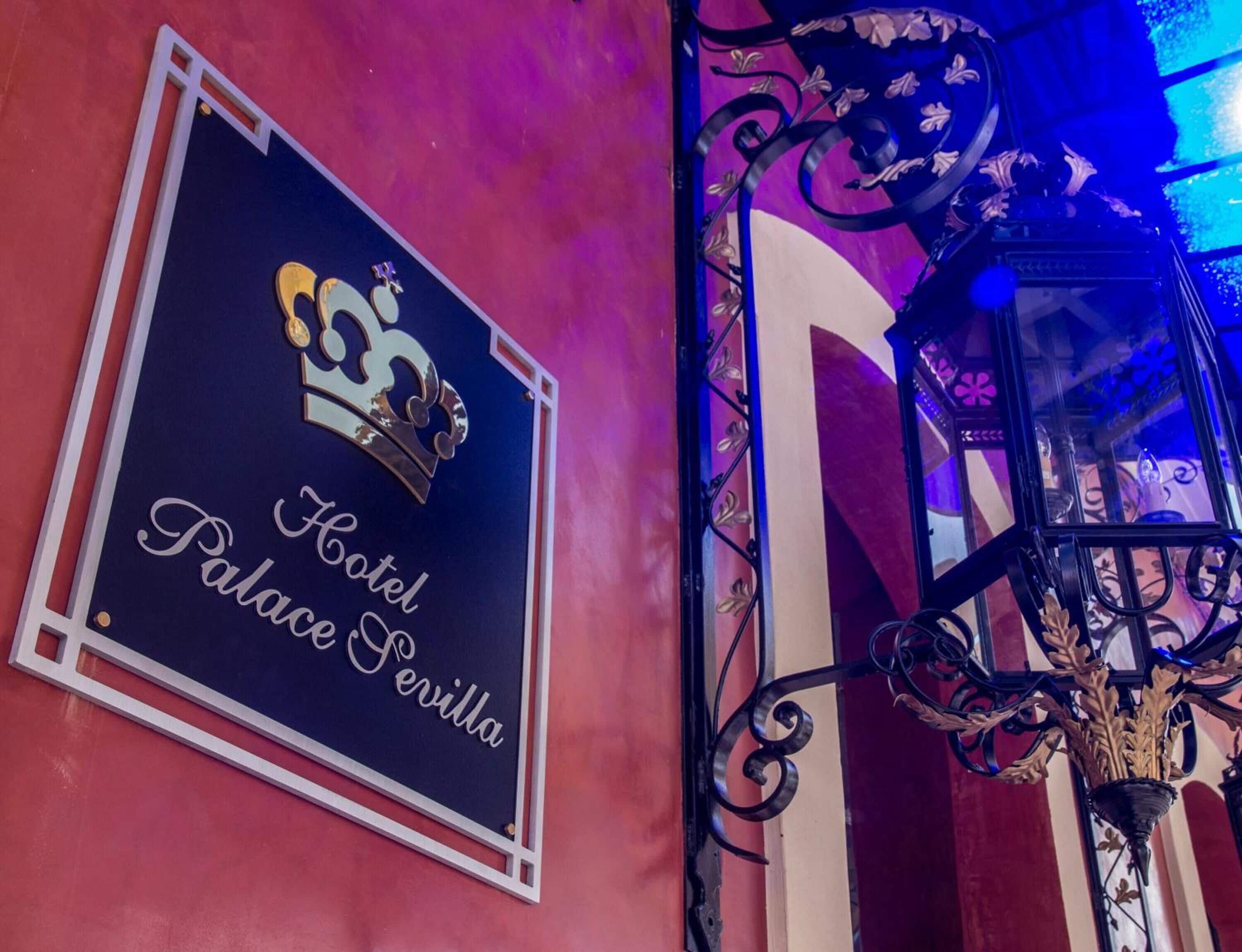 Cartell de l'Hotel Palacio de la Reina, amb un logotip de corona i el nom escrit amb lletra elegant.