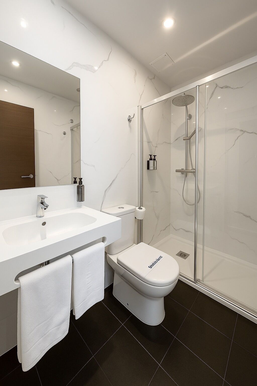 Un baño moderno con lavamanos, inodoro y ducha blancos.