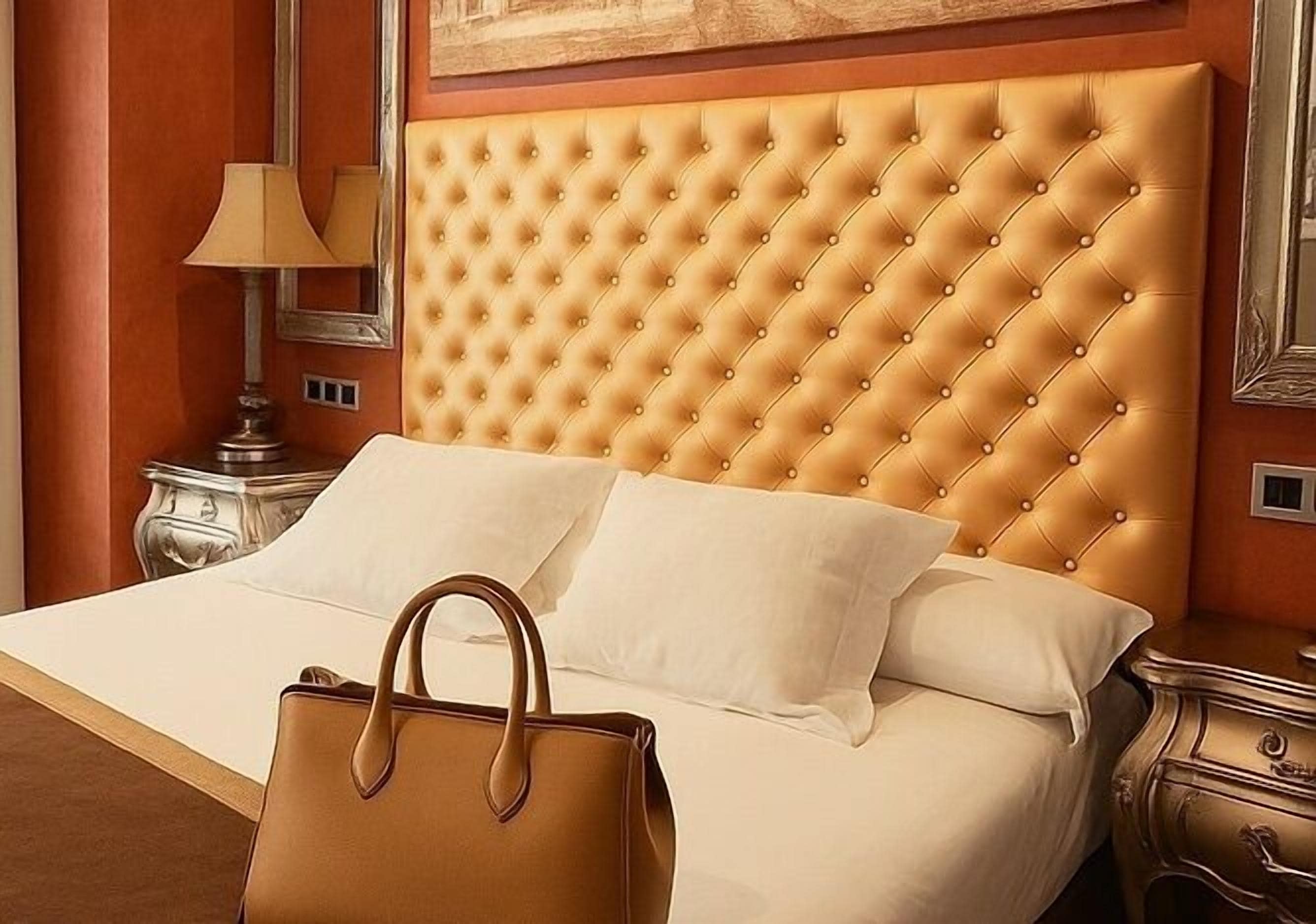 A bed with a tufted headboard, white bedding, and a brown handbag on the bed.
