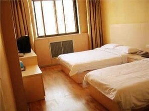A small, simple room with two single beds, a desk with a chair, and a window with curtains.