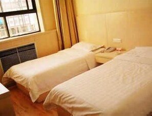 A hotel room with two single beds, a bedside table, a window with curtains, and a radiator.
