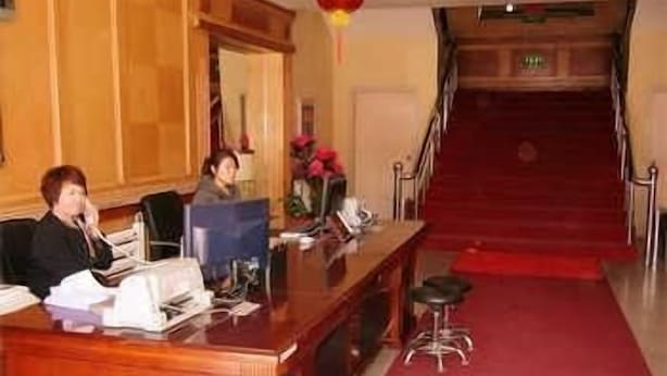 Ein Empfangsschalter mit Holzoptik, ein roter Teppich und eine Treppe, die zu einer oberen Etage führt.