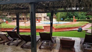 A covered outdoor seating area with lounge chairs and a pool in the background. - Afrikiko Riverfront Resort (Akosombo)