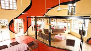 Un patio interior con mobiliario de mimbre y mesas, un ventilador de techo y vistas al área de estar exterior.