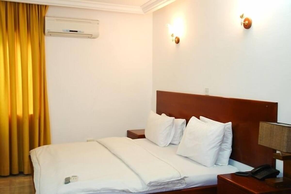 A hotel room with a bed, a nightstand, a lamp, and a wall-mounted air conditioner.