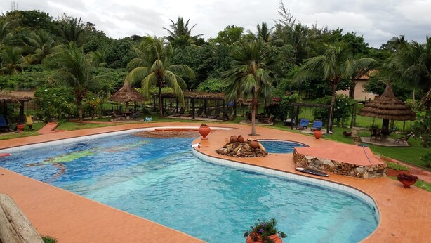 Una piscina con borde de piedra, rodeada de palmeras y un quiosco de techo de paja.