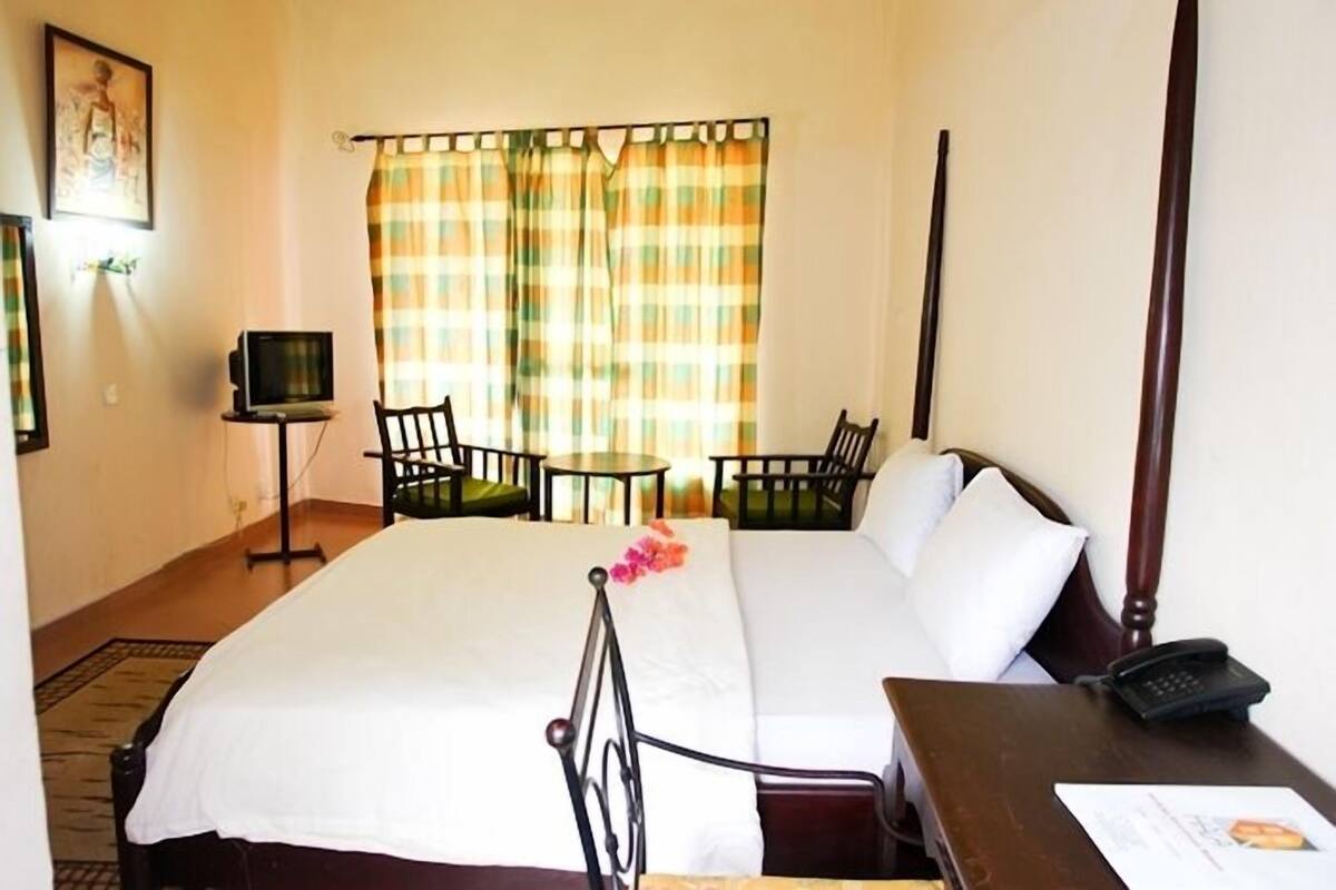 A hotel room with a bed, a desk with a phone, a chair, a small table with a TV, and curtains.