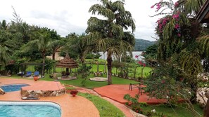 A pool area with a thatched-roof gazebo, lounge chairs, and a view of a lake.