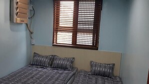 Un dormitorio con dos camas, una ventana con persianas y un equipo de aire acondicionado instalado en la pared.