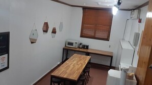 Una habitación pequeña y bien iluminada con una mesa y sillas de madera, una pizarra con escritura, un microondas y una ventana con persianas.