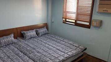 Uma cama de solteiro com cabeceira de madeira, roupa de cama cinza estampada e uma janela com persianas de madeira.