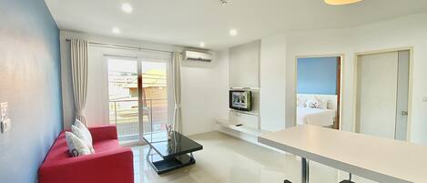 A modern living room with a red sofa, a black dining chair, a glass table, and a TV mounted on the wall.