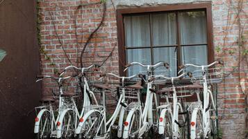 A row of white bicycles parked against a brick wall with a window and a door.