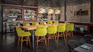 Een bar met een bakstenen muur, een houten toog en groene stoelen.